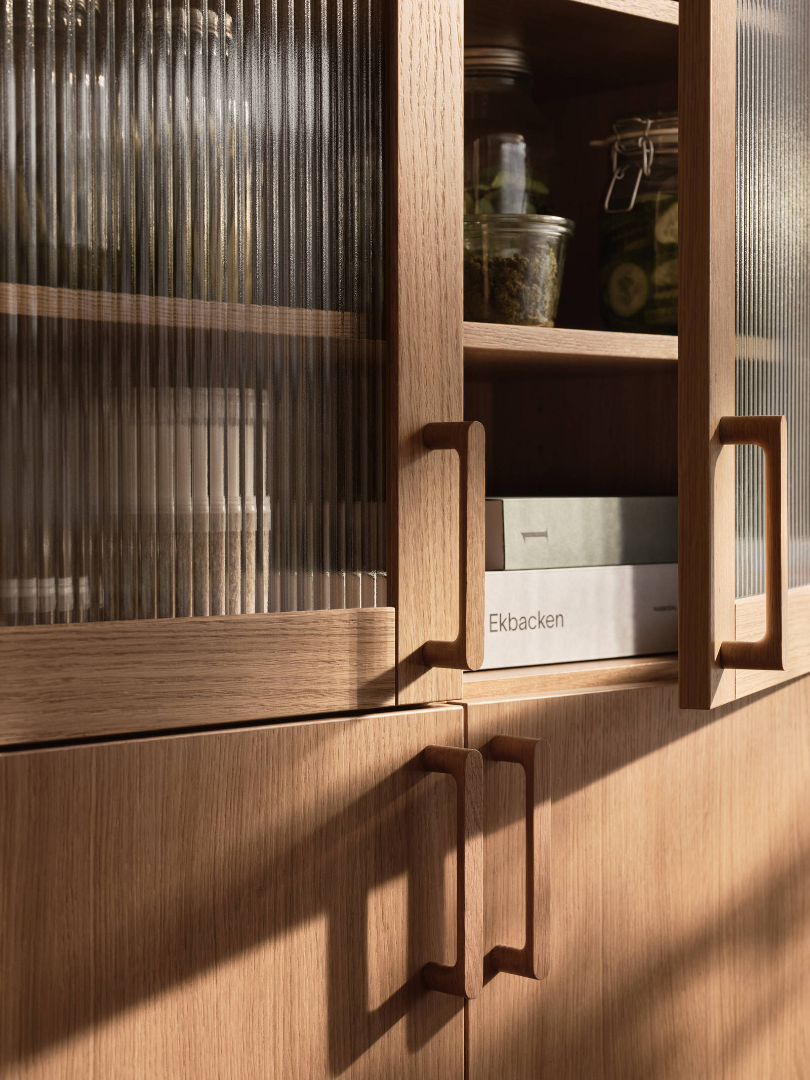 Öppnat vitrinskåp i Siri Barjes kök, räfflat glas i ram av ek, med matchande ekluckor på skåpen under och handtag i ek.