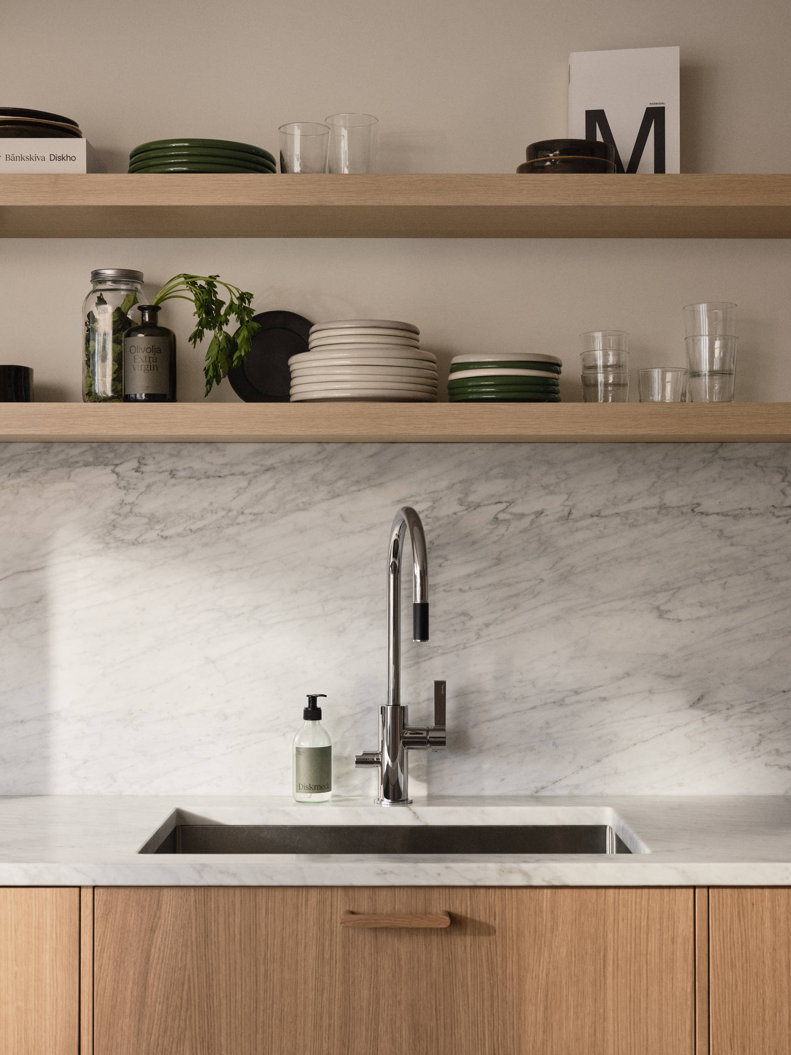 Öppna trähyllor ovanför köksbänk i Siri Barjes ek-kök från Marbodal, med bänkskiva och stänkskydd i marmor, svart diskho och blandare från Tapwell.
