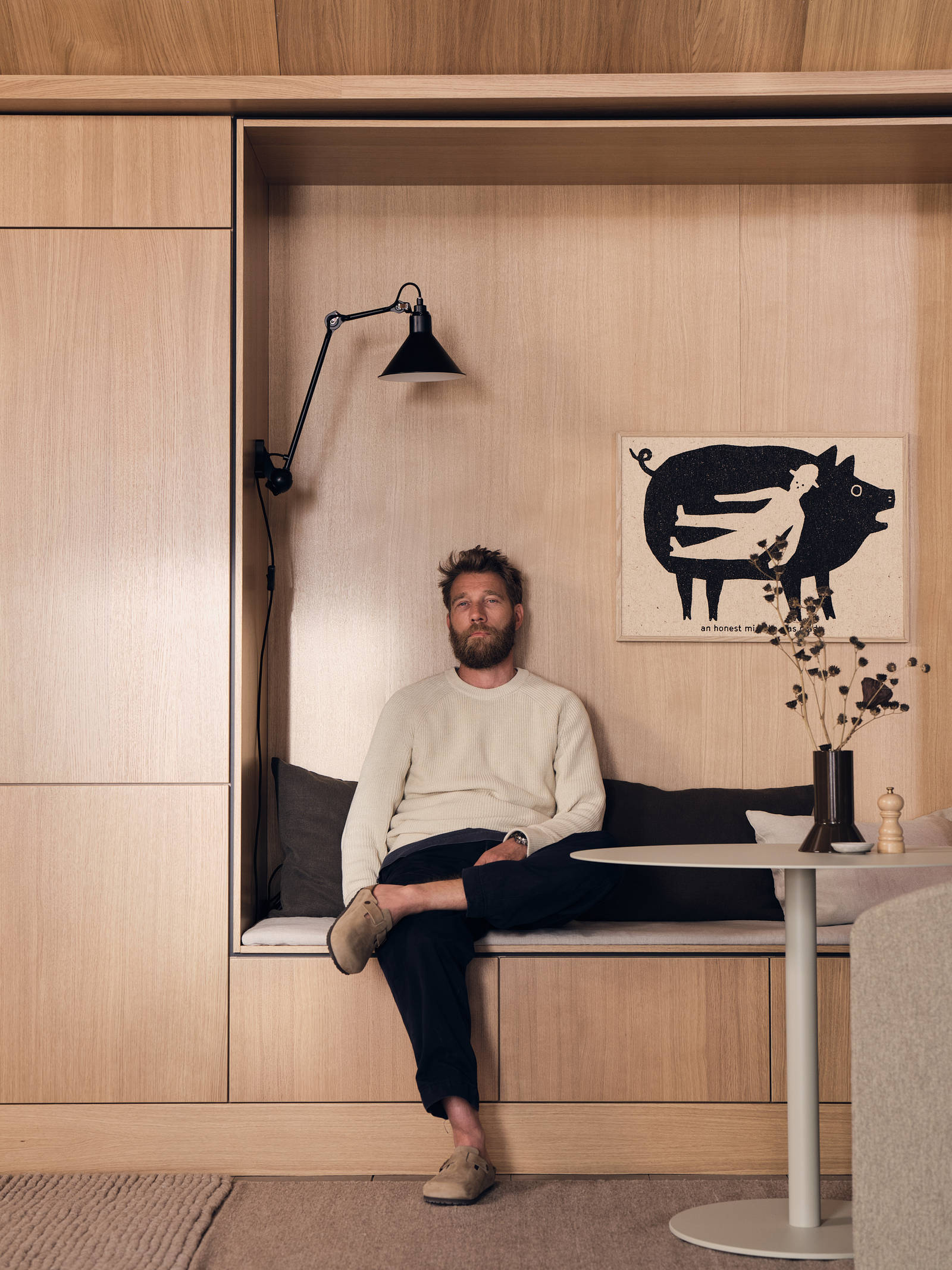 En man sitter på bänk i nischen i köket Ekbacken natur från Marbodal i ekfanér med vertikal träådring. Högskåp intill nischen som är inramad med en skuggning vilket skapar en arkitektonisk premiumkänsla.