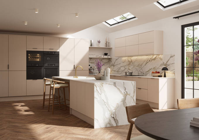 Fluted front kitchen Reed from Magnet in light warm neutral shade Shell, with a marbled splashback, worktop and decorative side on kitchen island with barstools and black handles, herringbone wood flooring.