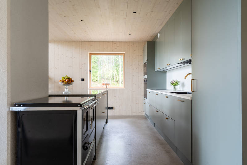 Vihreä keittiö Novartin luonnonvärisessä Havu-sävyssä, messinkinuppeilla, graniittitasoilla ja lasiovilla, joissa on alumiinikehykset keittiön altaassa.