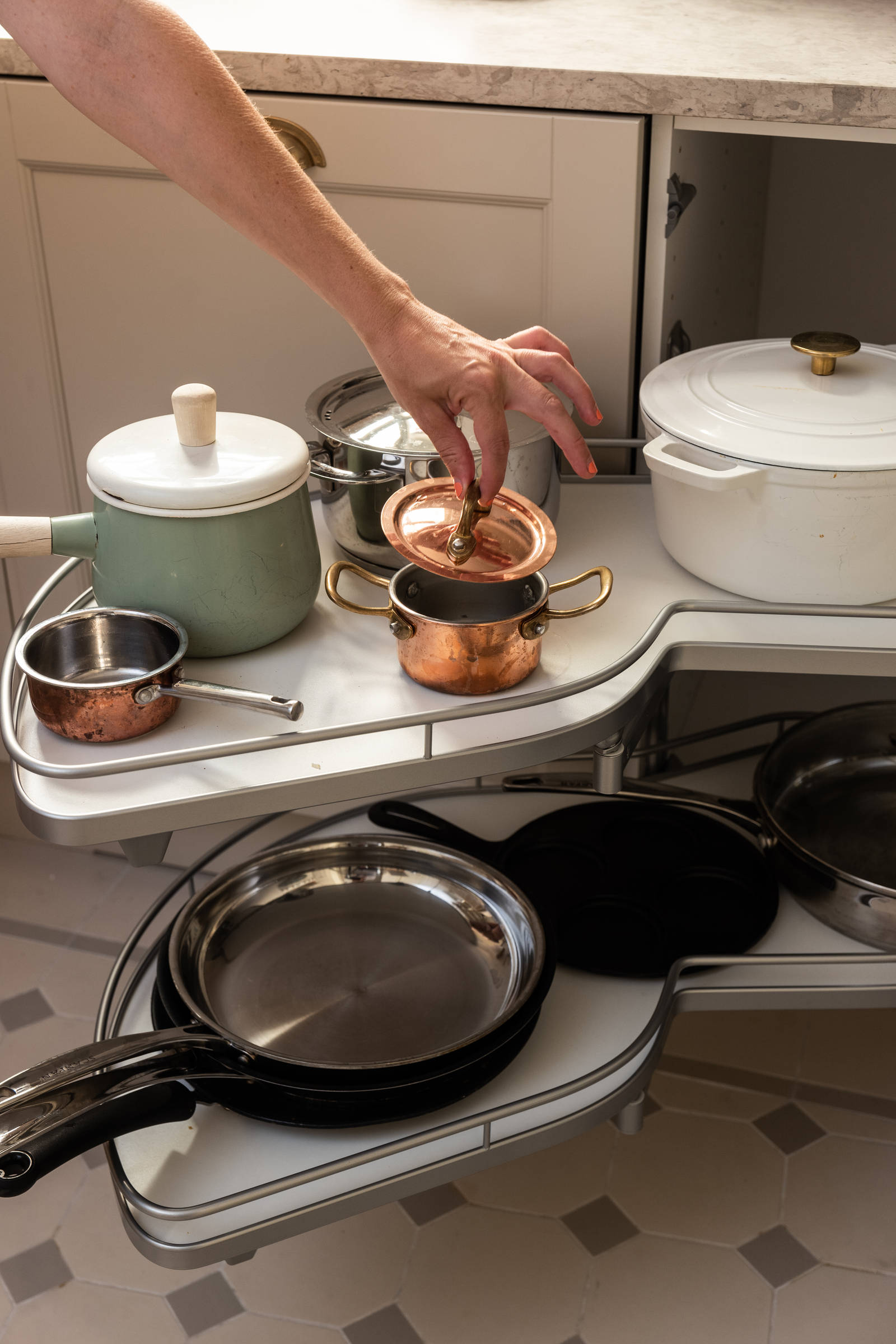 Sandra Beijer plockar upp locket från en liten kastrull i hörnskåpet le mans i sitt kök från Marbodal, lantliga luckan Fagerö i beige kulören Sand, med bronsfärgade handtag.