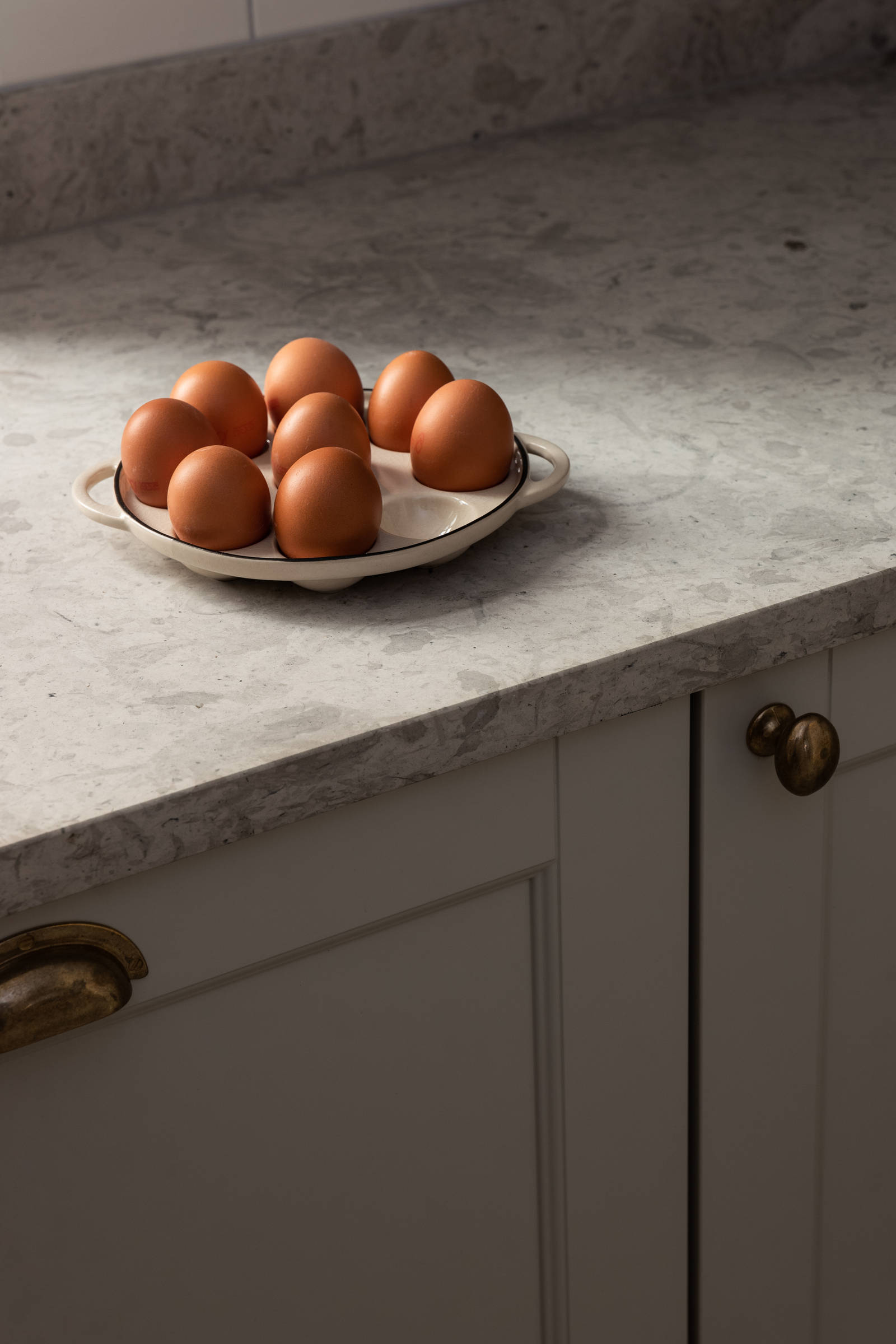 Närbild på köksbänken i Sandra Beijers kök från Marbodal med lantliga luckan Fagerö i beige kulören Sand, bronsfärgade handtag och knoppar, bänkskiva i kalksten och ett fat med naturfärgade ägg på köksbänken.