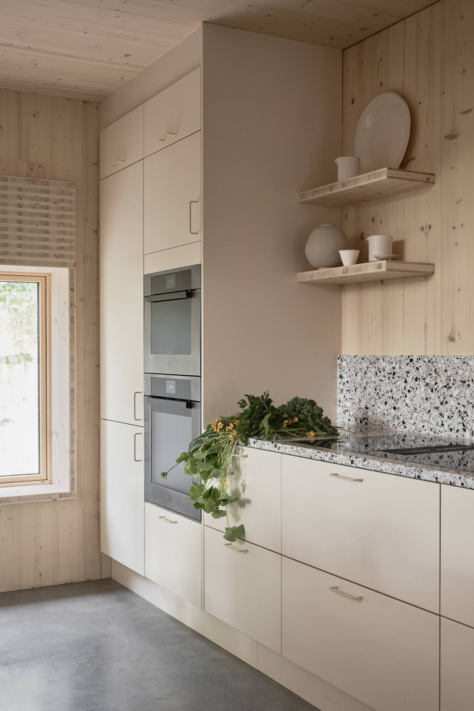 Högskåp med inbyggda ugnar, öppna vägghyllor och terrazzo-bänkskiva med matchande stänkskydd i Edd Ruchtons Grand design kök i beige Arkitekt Plus-kök från Marbodal