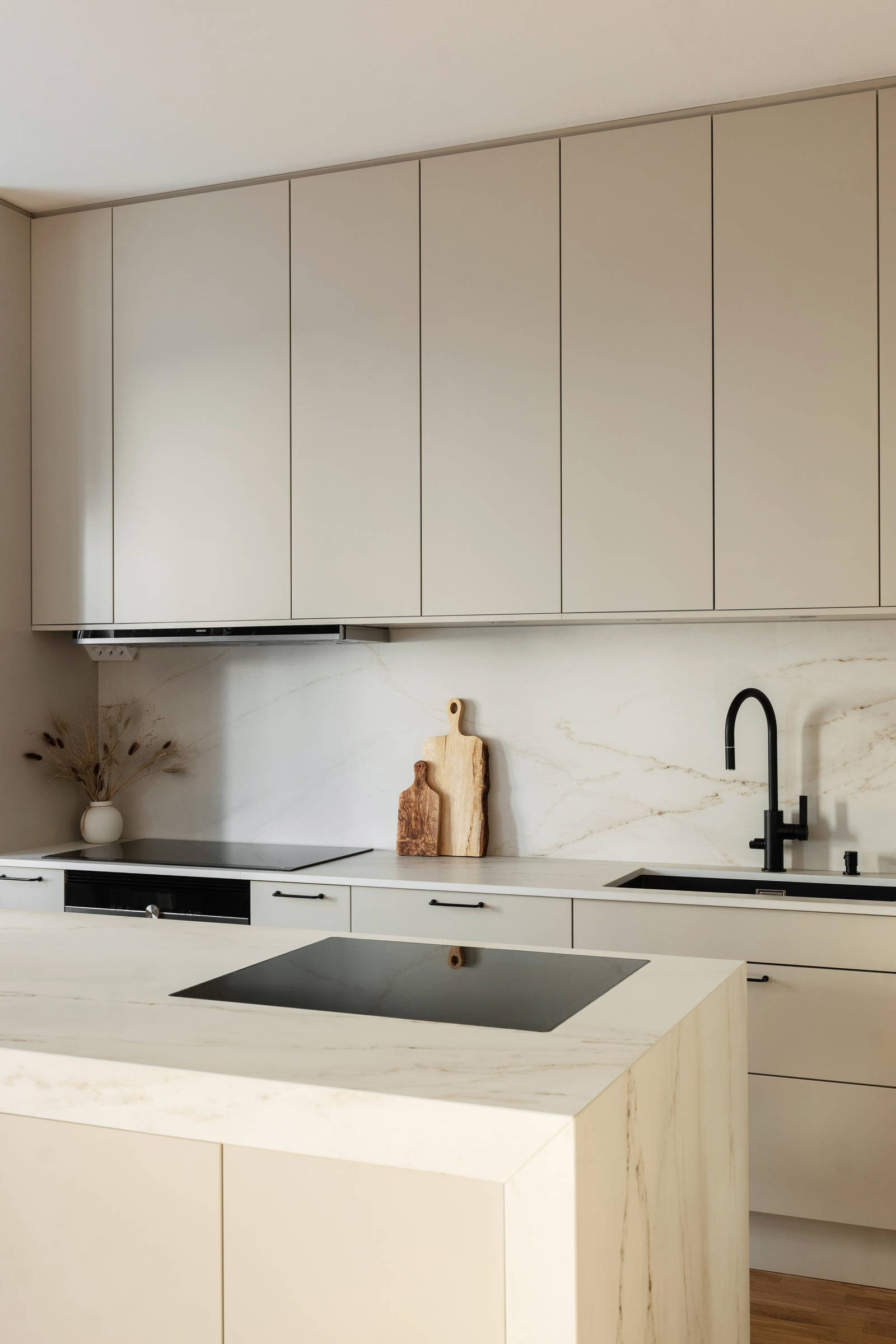 Spishäll i köksö, matt svart blandare och diskho i Filip Poons kök från Marbodal, Arkitekt Plus Sand med svarta handtag och Dekton bänkskiva samt stänkskydd