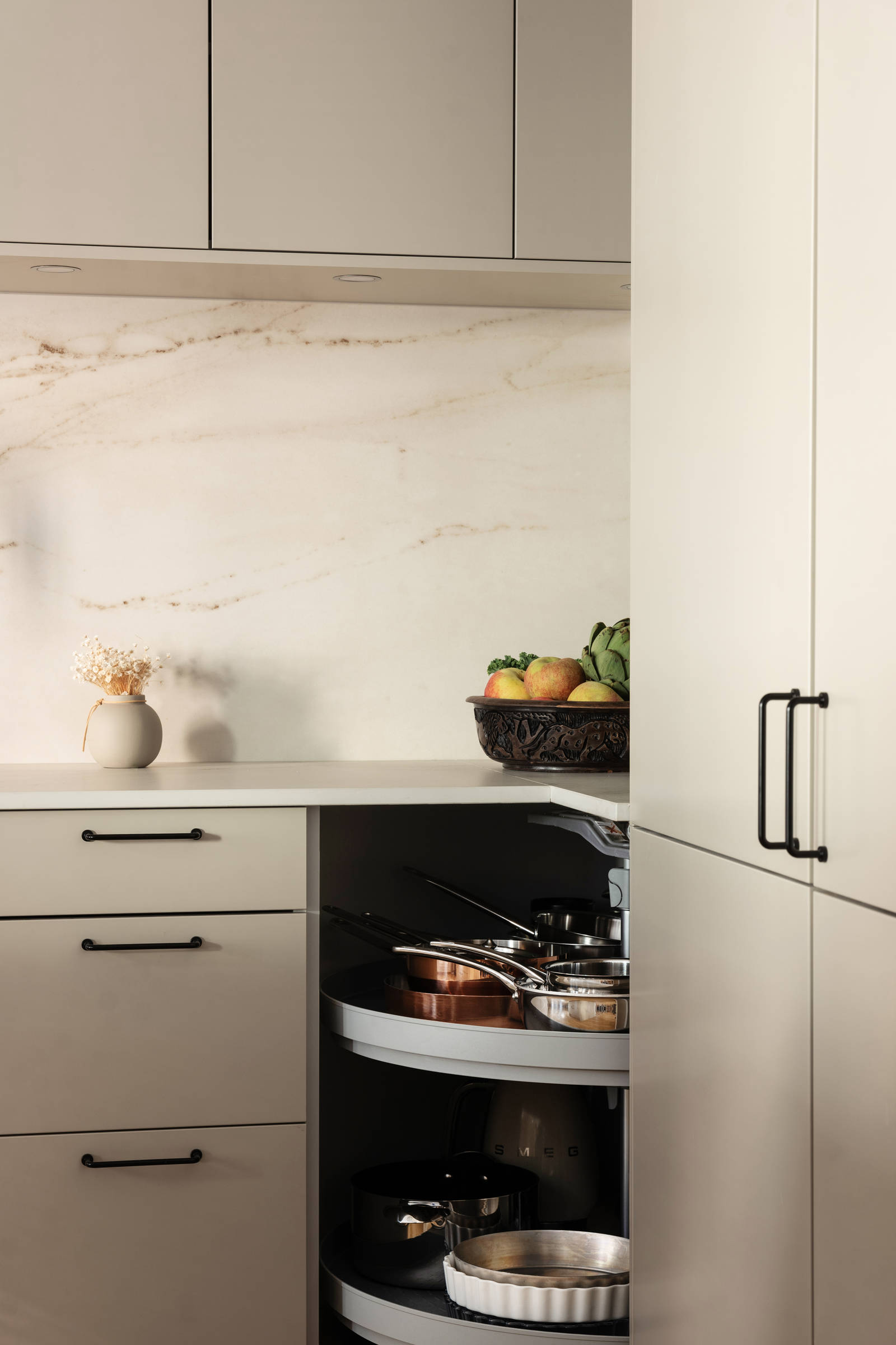 Öppet hörnskåp med karusellhyllor i Filip Poons kök från Marbodal, Arkitekt Plus Sand med svarta handtag och Dekton bänkskiva.