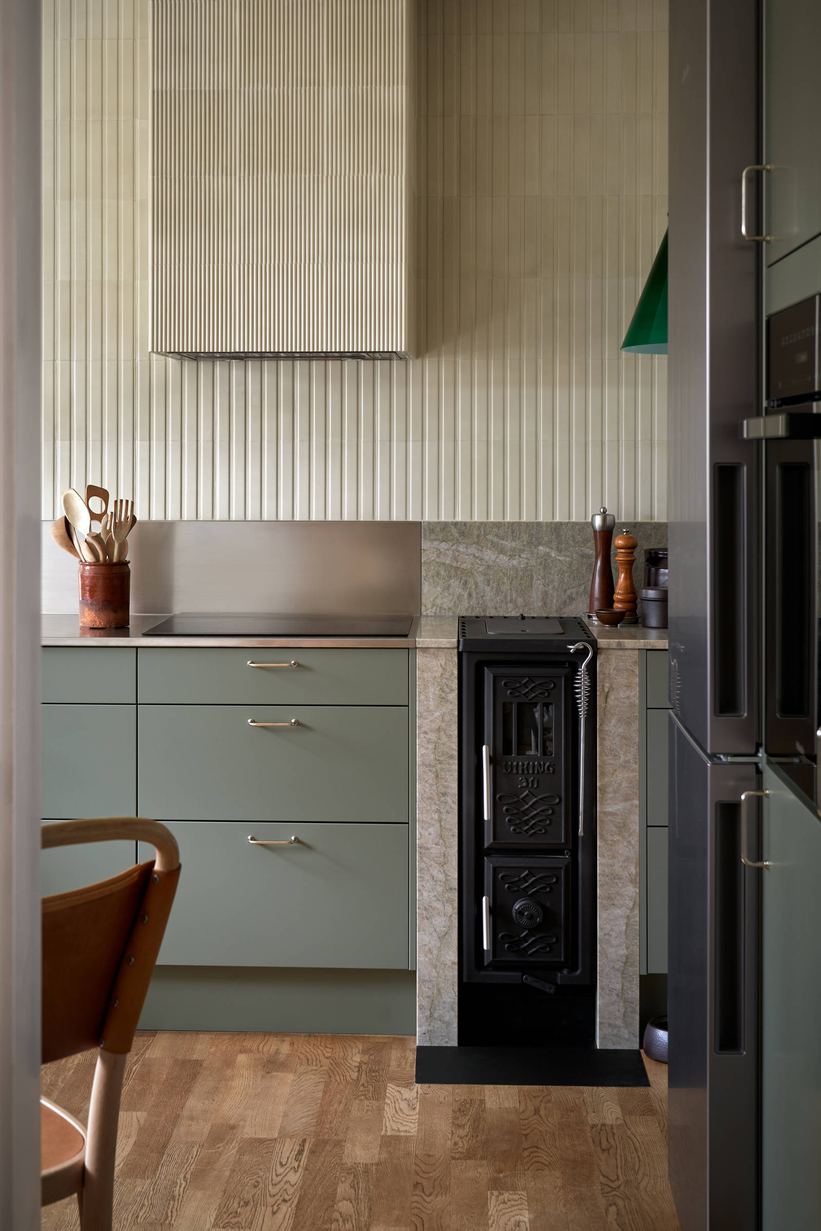 Gröna köket Arkitekt plus i kulören Tall med en vedspis och bänkskiva i kvartsit