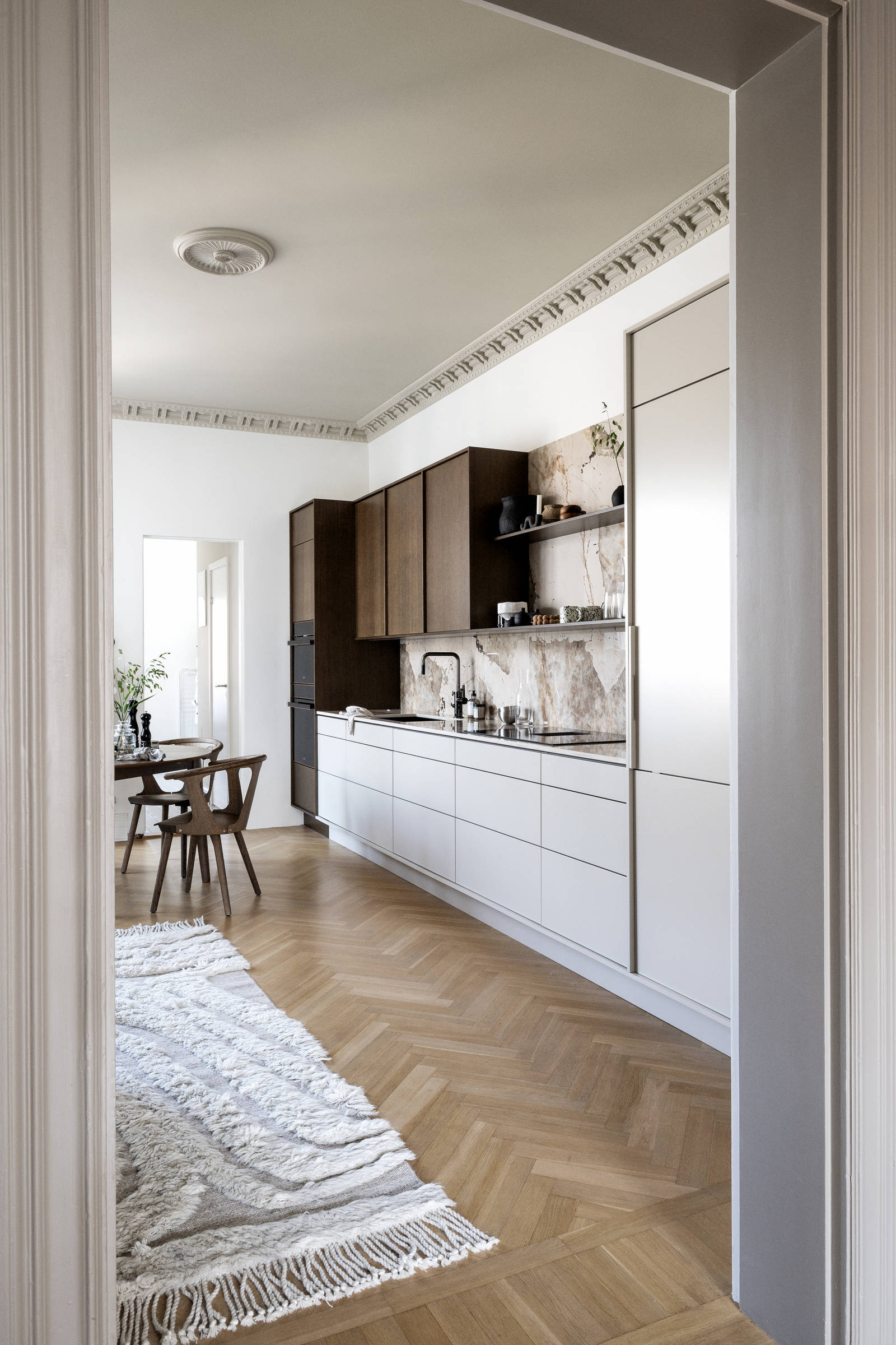 Køkken med en kombination af køkkenbænk i beige Athena Sand med overskabe og højskabe i Forever Oak fineret egetræslåge i brunbejdset fra INVITA, bordplade og stænkplade der matcher og åbne væghylder i brunbejdset eg finer.