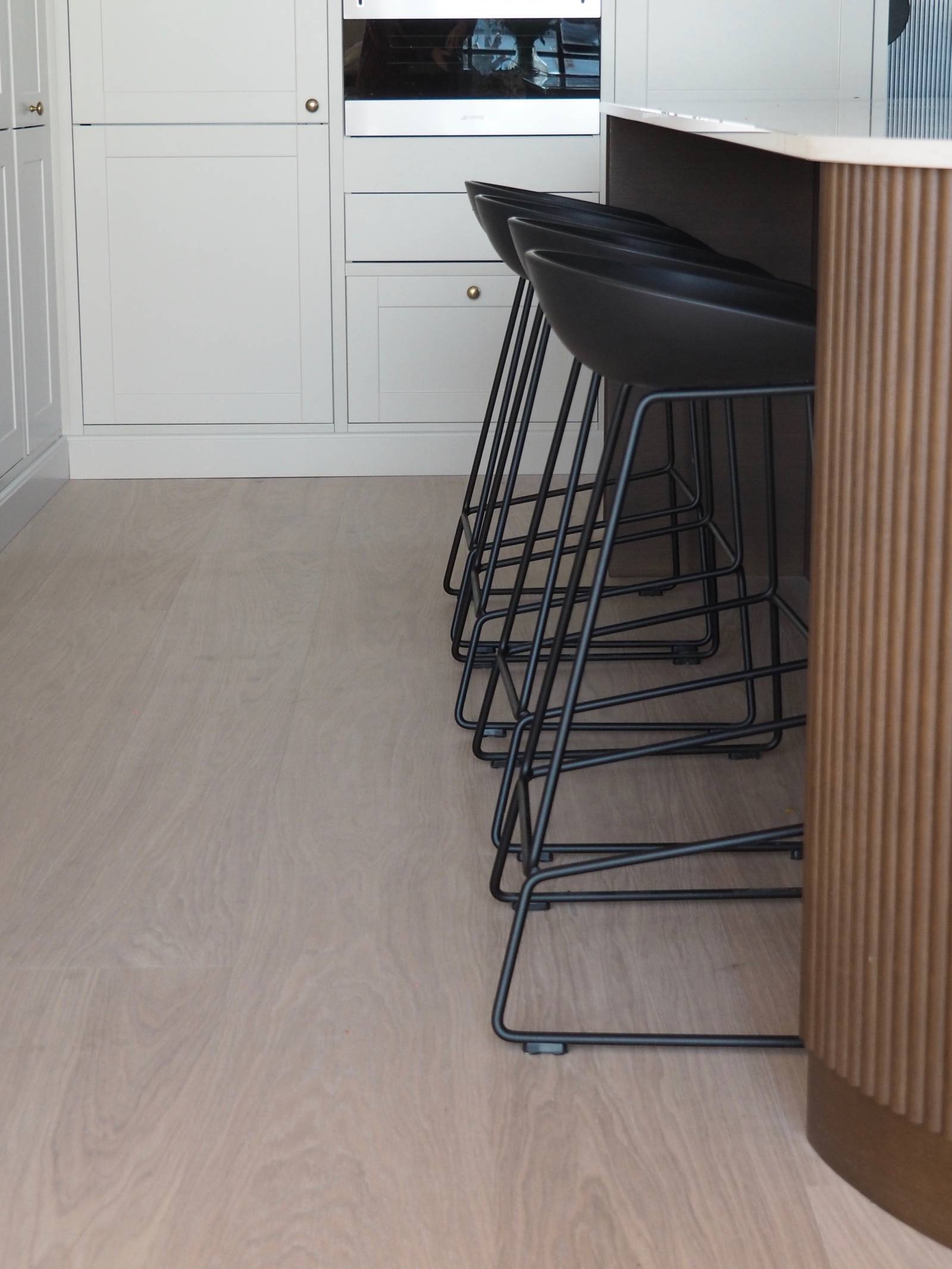 Enden af ​​den afrundede køkkenø med mørkt træpanel, Dekton Taga bordplade og sorte barstole