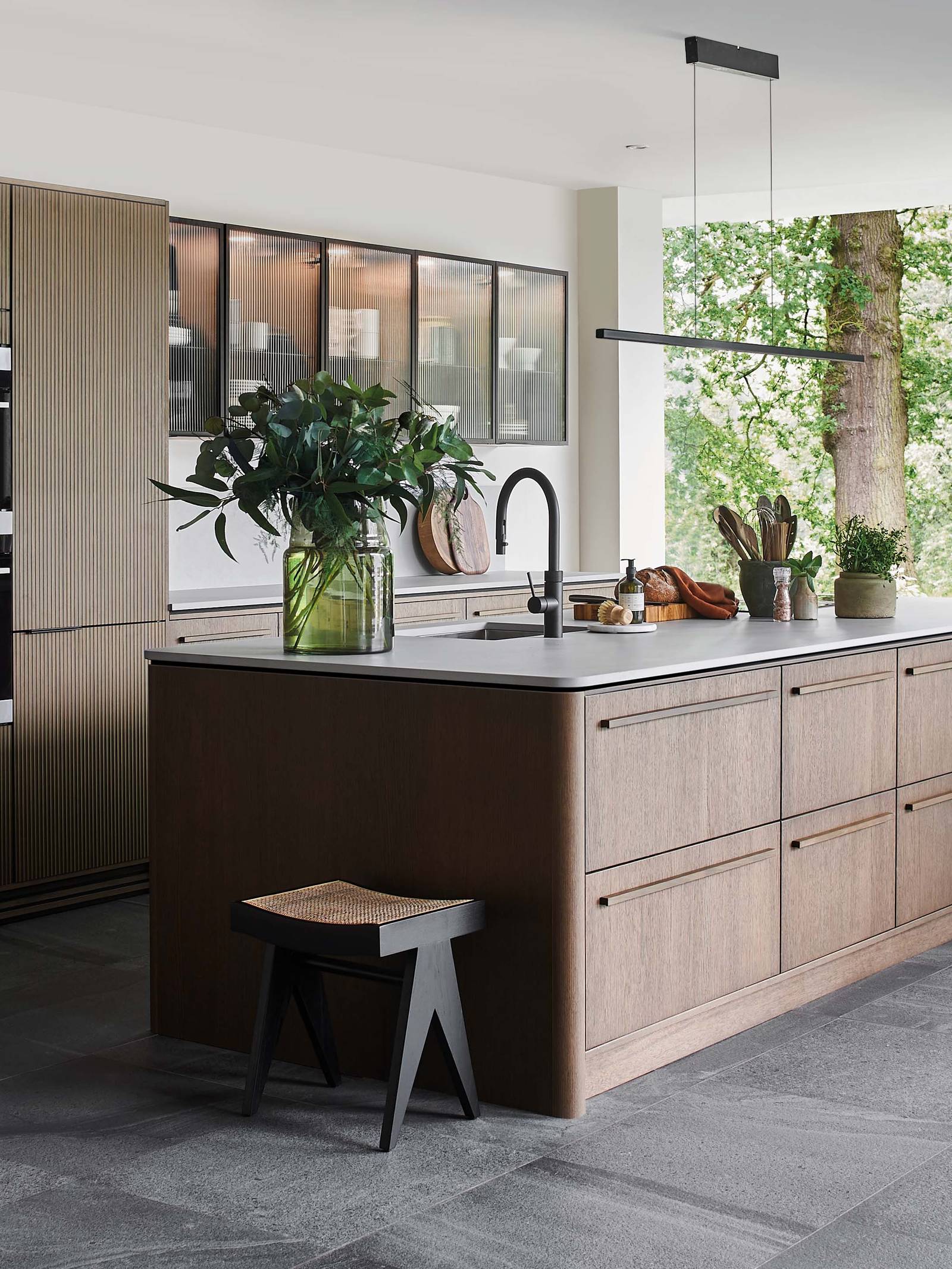 Nordic Nature open plan kitchen and living room, a woman sitting in a comfortable chair by the fireplace.