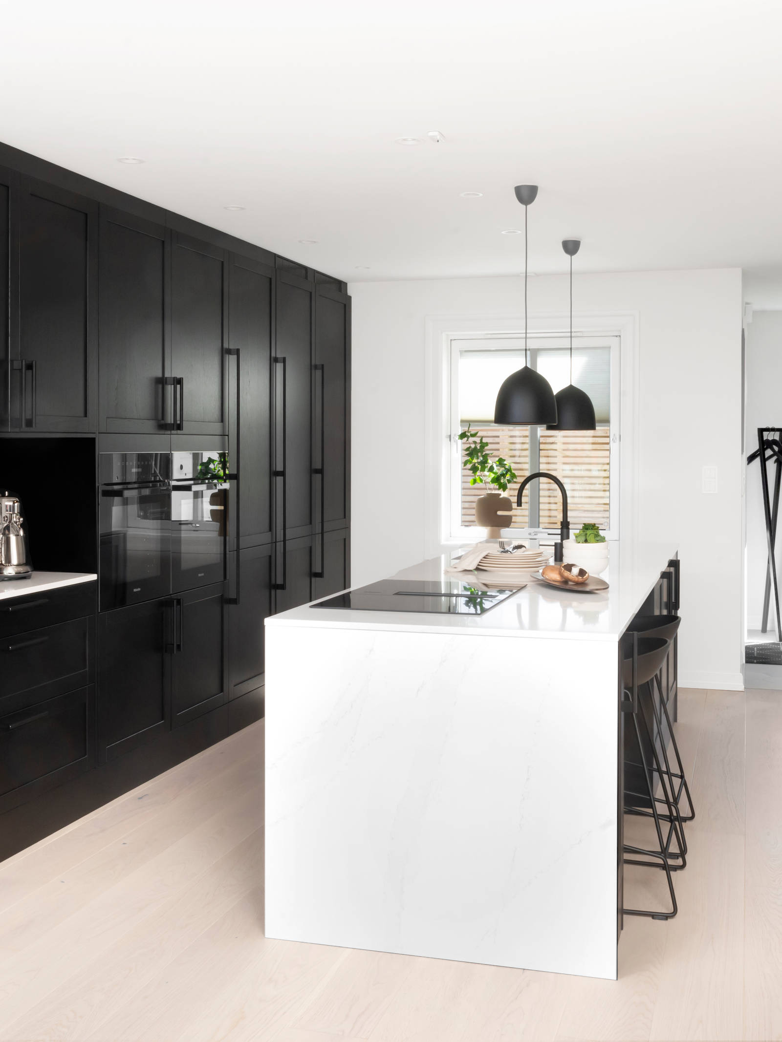 Et nydelig svart kjøkken i lun eik med kjøkkenøy dekket av lys komposittstein og stilige matt-svarte håndtak.