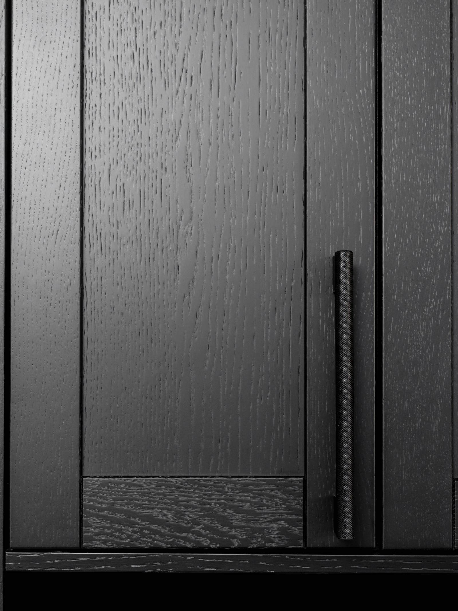 Et nydelig svart kjøkken i lun eik med kjøkkenøy dekket av lys komposittstein og stilige matt-svarte håndtak.