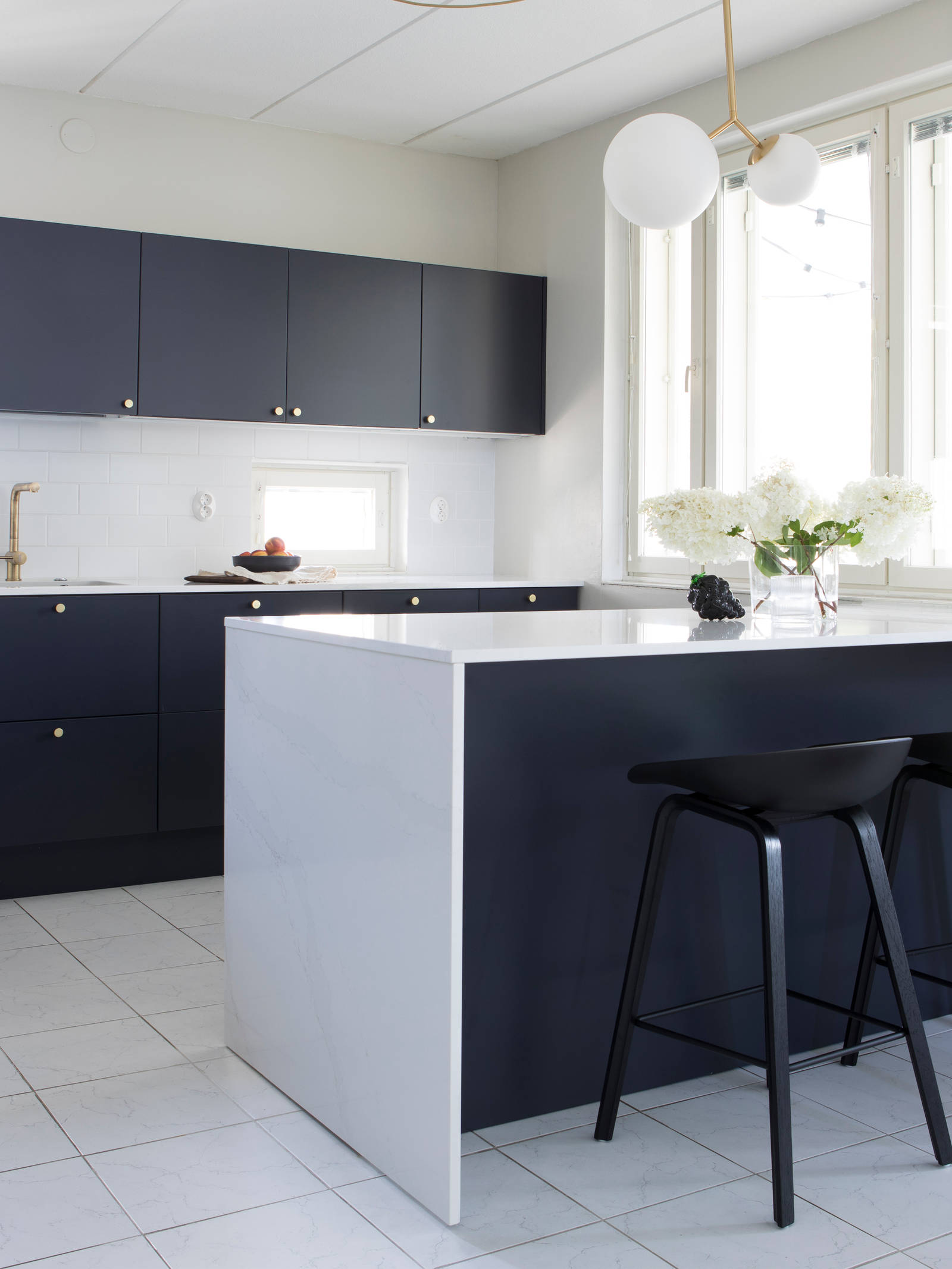 Tummansininen Meri maalattu sileä keittiö, jossa valkoinen marmoroitu työtaso ja siihen sopiva roiske, keittiösaareke istuinalueella, messinkinupit ja messinkihana