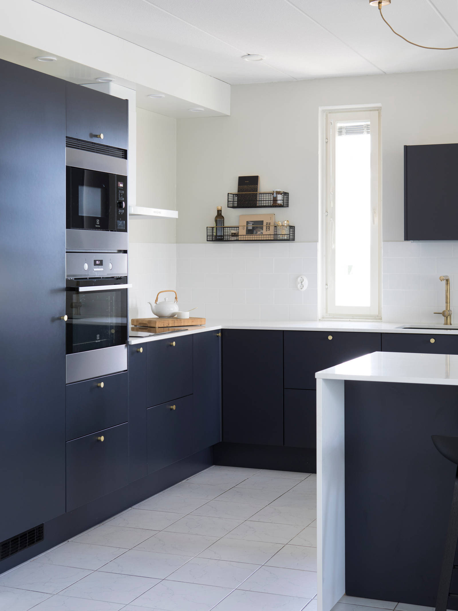 Tummansininen Meri maalattu sileä keittiö, jossa valkoinen marmoroitu työtaso ja siihen sopiva roiske, keittiösaareke istuinalueella, messinkinupit ja messinkihana