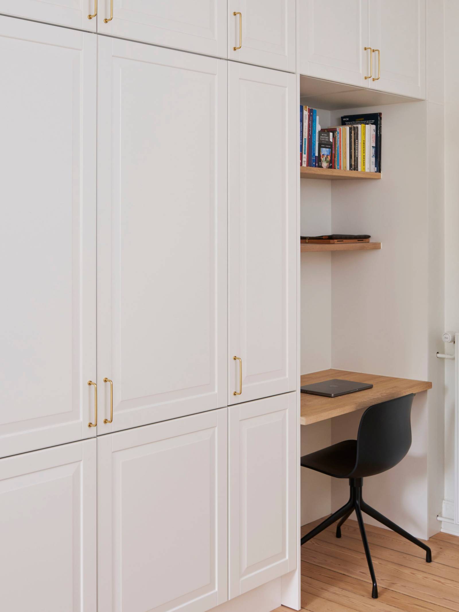 Hvid garderobe Nordic Frost fra INVITA med fyldningslåger og messinggreb, med indbygget bordplade med stol og væghylder til hjemmekontoret