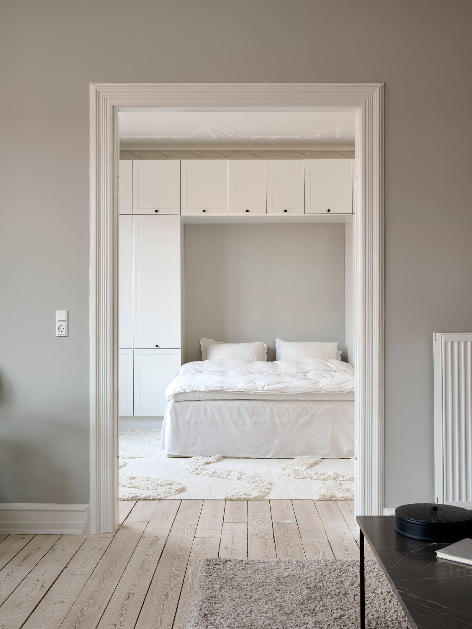 Hvid tidløs garderobe Square Sand fra INVITA omkring en seng med en kommode over, sorte greb på karmdøren