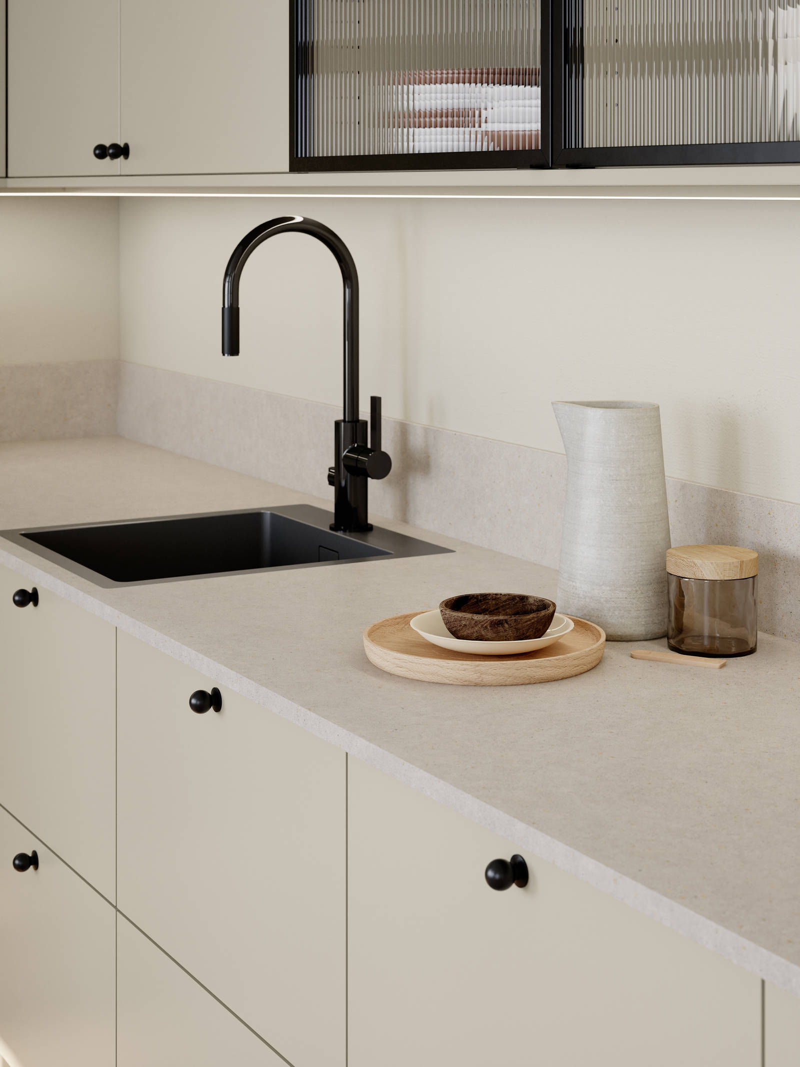 Beige melaminkök med svarta knoppar, svart blandare och vitrinlucka med svart aluiminiumram och räfflat glas.