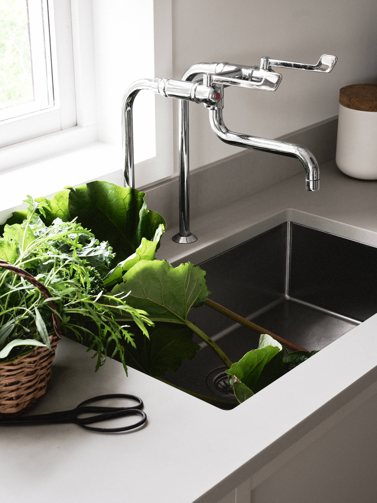 Närbild på diskho i rostfritt stål och matchande kran i Lotta Agatons kök från Marbodal, med bänkskiva i ljusgrå sten och inramade luckor i kulören Sand.