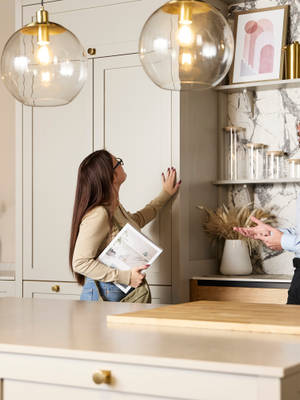Woman holding a brochure and feeling a Shaker front with her hand while speaking to a kitchen designer in a Magnet Showroom.