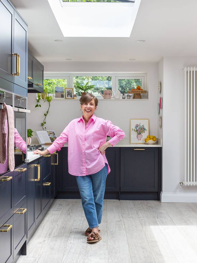 Marina smiling in her bold and welcoming dark blue Dunham Midnight kitchen from Magnet, with tall cabinets and open shelves.