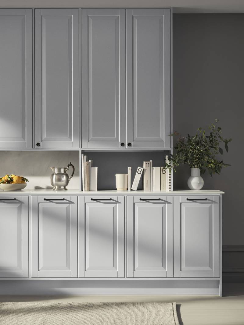 Lys grå landkøkken Nordic Sky fra INVITA med fyldningslåger, sort håndtag, vitrineskab med sprosselåger og hvid marmor laminatbordplade