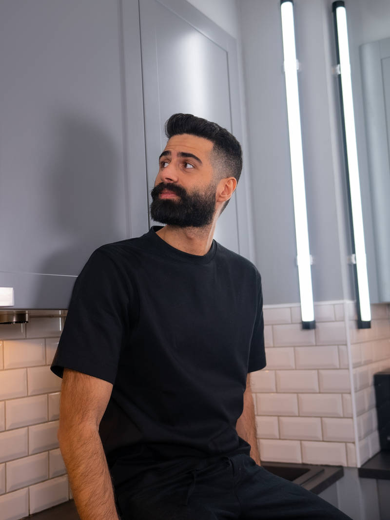 Simon Kafi sitter på köksbänken i sitt kök från Marbodal, mörkgrå ramlucka Form Åska med svarta handtag och svart bänkskiva med stänkskydd i vitt kakel