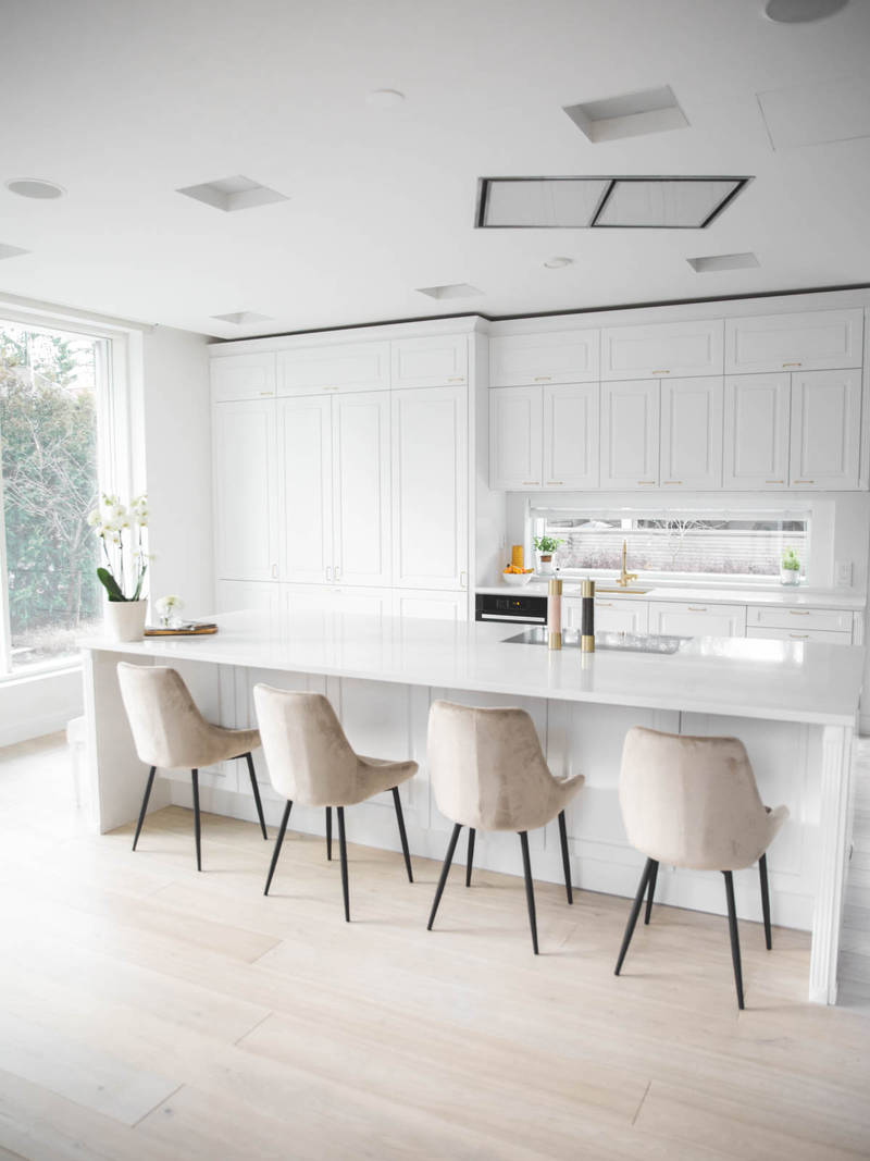 Valkoinen keittiö, jossa perinteiset maalatut karmiovet, messinkikahvat ja marmoroitu työtaso, keittiösaareke istuimilla.