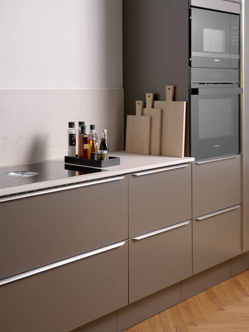 Minimalistisk brun køkken Newline Bark fra INVITA med indbygningsovne i højskabe, diskret greb i stål og lys beige bordplade med matchende splashback