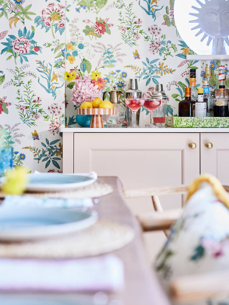 Cocktail corner in Sophie Robinsons maximalist Ludlow kitchen from Magnet, with a dining room table in foreground, floral pattern wallpaper.