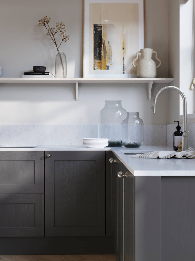 Ludlow, a traditional Shaker-style premium feel kitchen range with a visible woodgrain on its panelled doors here shown in the dark grey shade Charcoals styled with steel knobs, steel tap, a white marbled worktop with matching splashback.