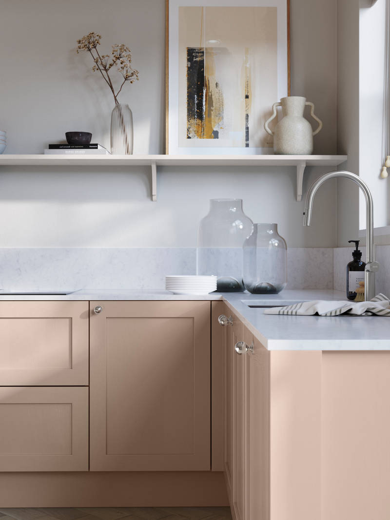 Wardley Chalk Blush kitchen cabinetry with steel knobs, steel tap, white marbled worktop and matching backsplash. An open shelf on the wall above cabinets with ceramics and a vase of flowers.