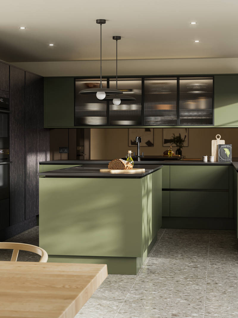 Integra Soho Tailored Green kitchen and kitchen island with contrasting dark wood Portobello Etna, black accessories, integrated ovens in tall cabinets, Dekton worktop and fluted glass vitrin wall cabinets with wood dining room table in foreground.