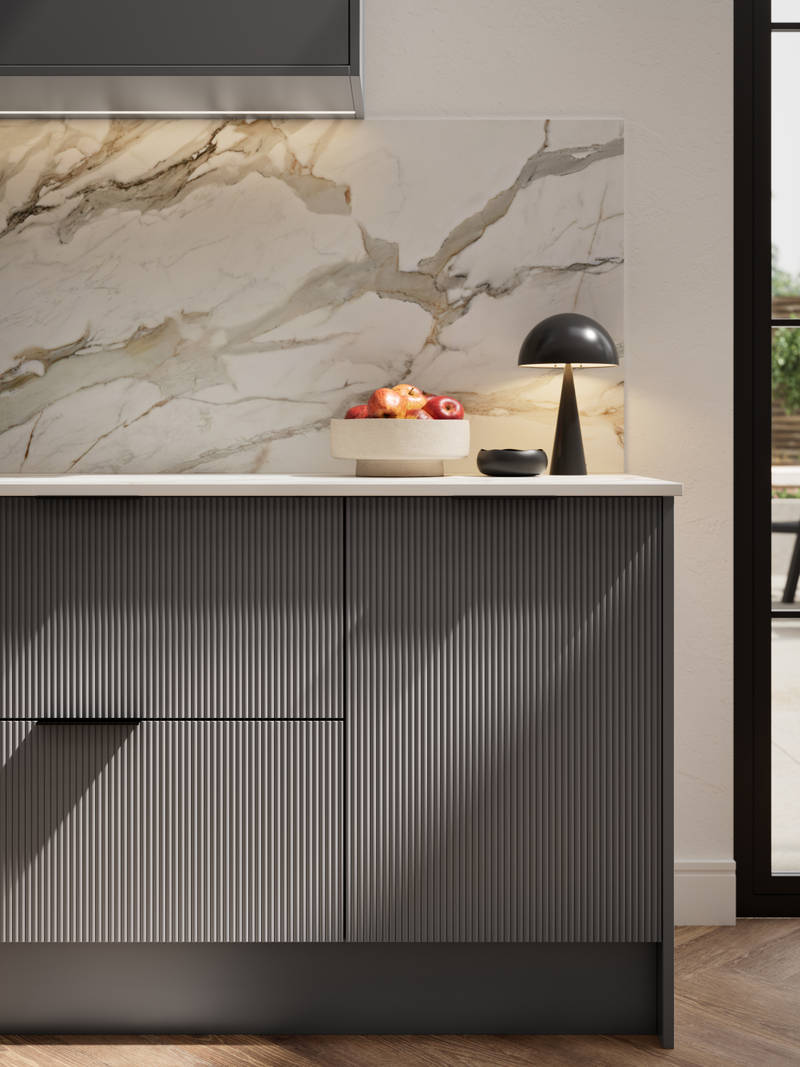 Fluted front kitchen Reed from Magnet in dark grey shade Charcoals, with a marbled splashback and black handles, herringbone wood flooring.