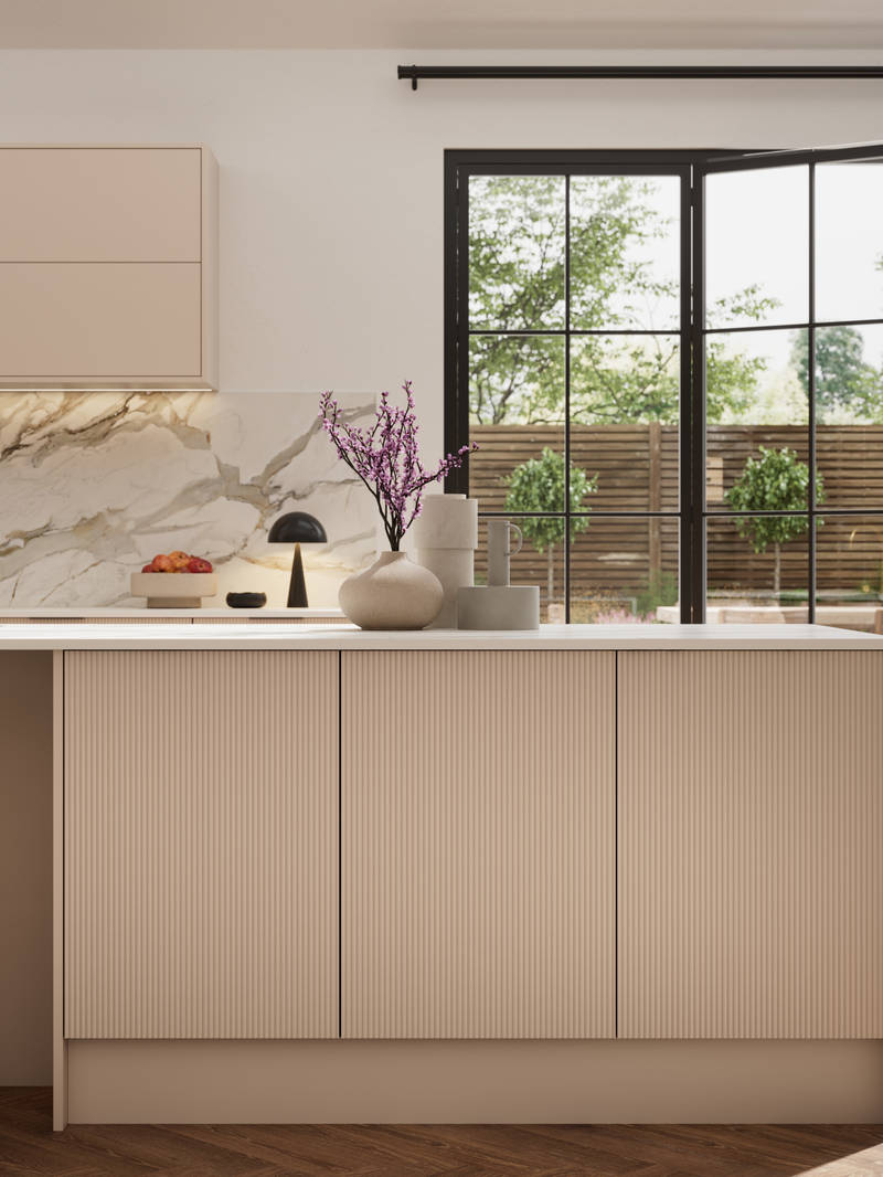 Fluted front kitchen Reed from Magnet in light warm neutral shade Shell, with a marbled splashback, worktop and decorative side on kitchen island with barstools and black handles, herringbone wood flooring.