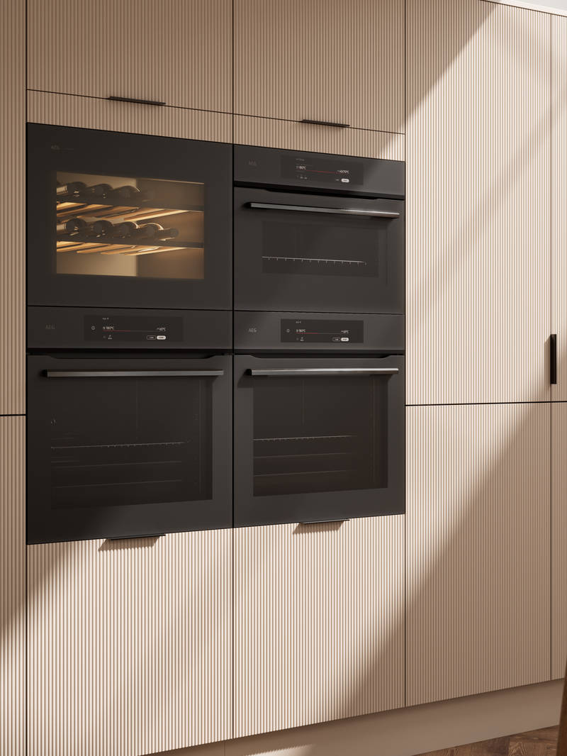 Fluted front kitchen Reed from Magnet in light warm neutral shade Shell, tall cabinets with appliances like ovens and a wine cooler, black handles
