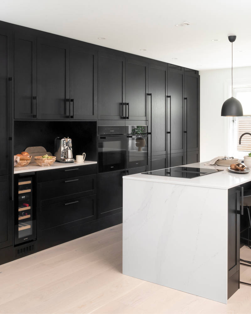 Et nydelig svart kjøkken i lun eik med kjøkkenøy dekket av lys komposittstein og stilige matt-svarte håndtak.