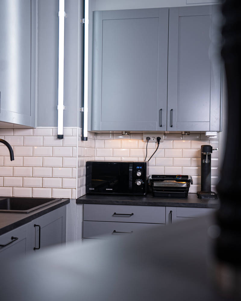 Mörkgrå ramlucka Form Åska med svarta handtag och svart bänkskiva med stänkskydd i vitt kakel i köket hemma hos Simon Kafi