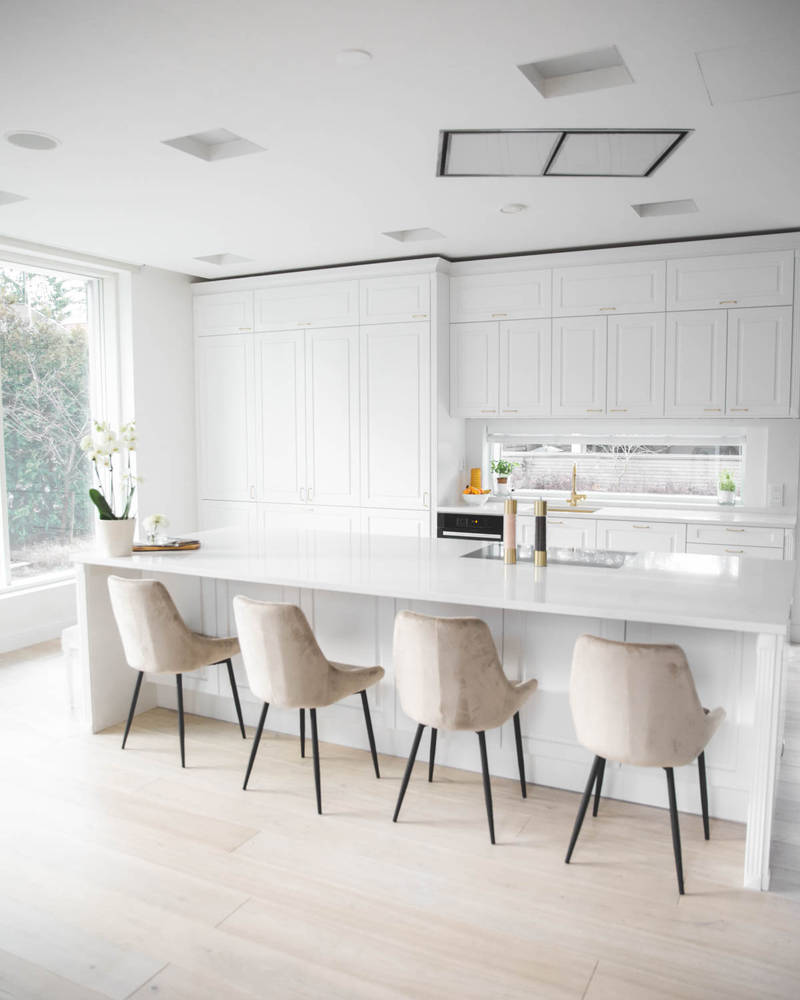 Valkoinen keittiö, jossa perinteiset maalatut karmiovet, messinkikahvat ja marmoroitu työtaso, keittiösaareke istuimilla.
