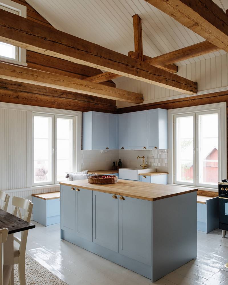 Keittiössä keittiösaareke, karmiovet erikoissävyssä NCS S 1020-R90B 1800-luvun hirsitalossa, tammitasot, posliinitiskiallas ja messinkihana.