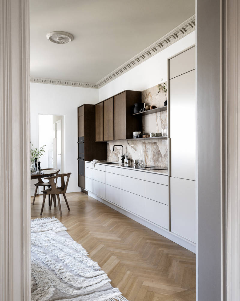 Køkken med en kombination af køkkenbænk i beige Athena Sand med overskabe og højskabe i Forever Oak fineret egetræslåge i brunbejdset fra INVITA, bordplade og stænkplade der matcher og åbne væghylder i brunbejdset eg finer.