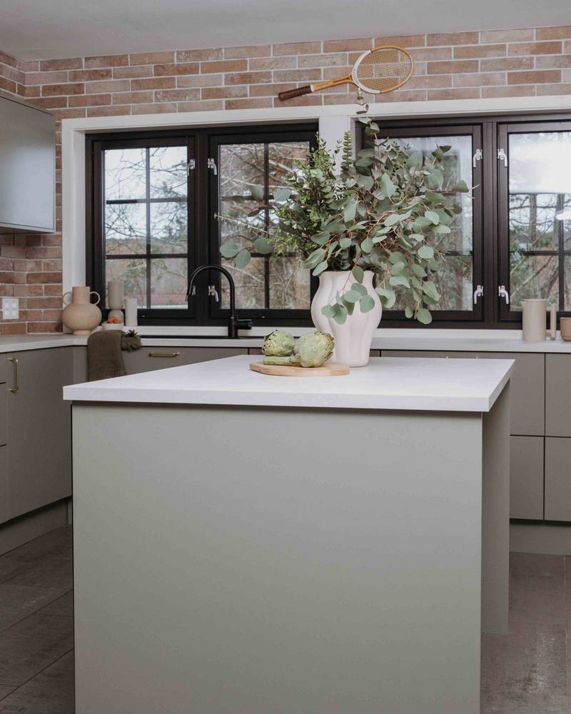 En keramikkvase med grønne planter og et skjærebrett i tre med ertebelger på kjøkkenbenken i Stine Hartmanns Uno Furu kjøkken fra Sigdal