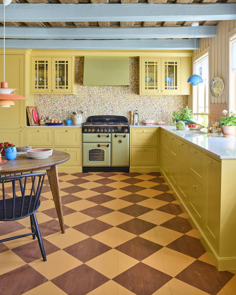 Landlig rammekjøkken Scala Inframe fra Sigdal som gir en snekkerbygged preg, vitrineskaber, Falcon Classic Olive green komfyr med gassbrennere og Røroshetta Grue ventilator i samma fargekode, rutete gulv