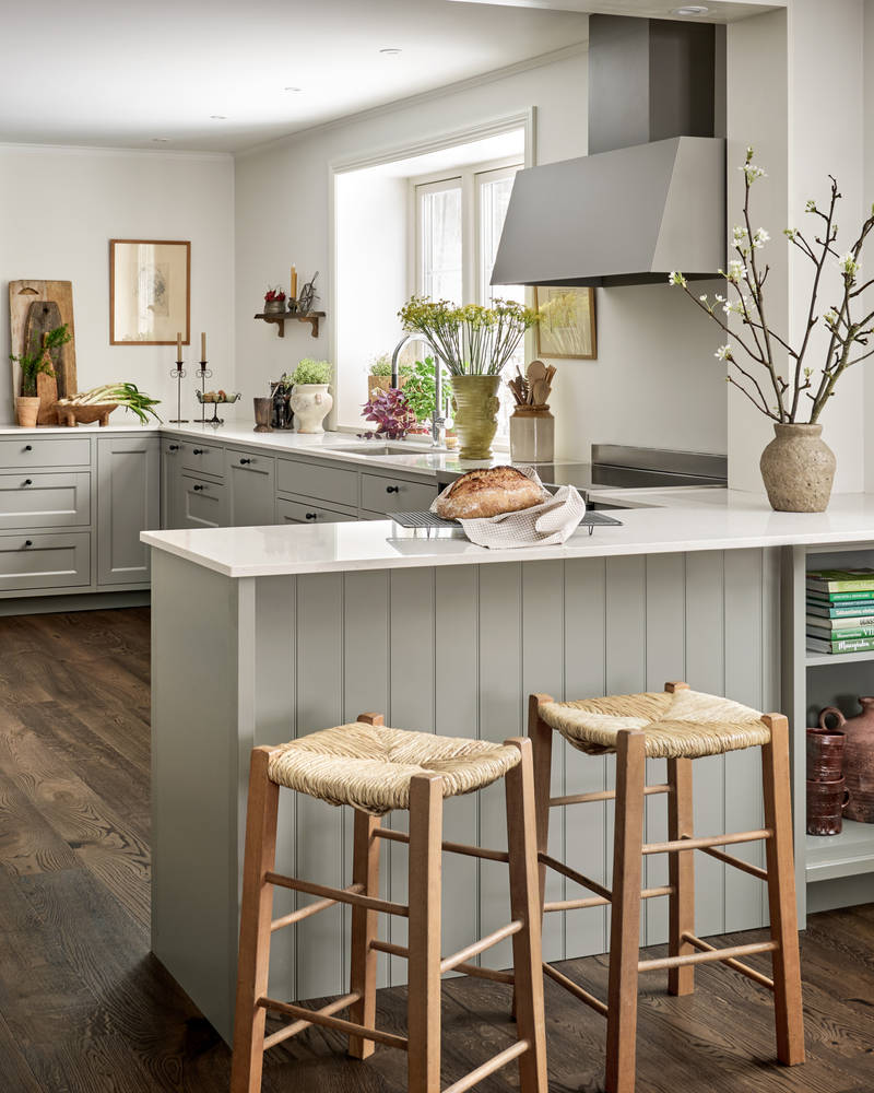 Malin Berghagens kök från Marbodal, lantliga Fagerö i kulören Frö med vit och grå marmorerad bänkskiva, med halvt fristående köksö med två barstolar och en öppen hylla för böcker och keramik.