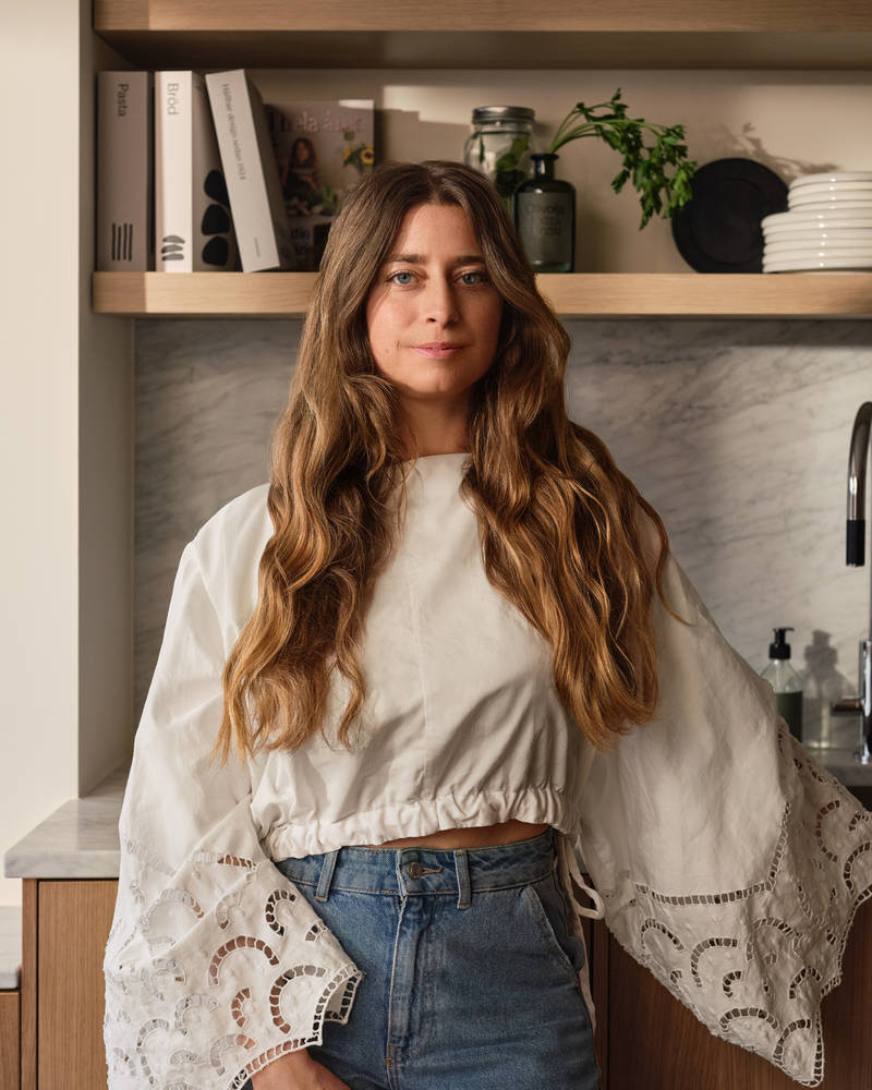 Siri Barje iklädd en ljus stor blus och jeans i sitt kök från Marbodal.