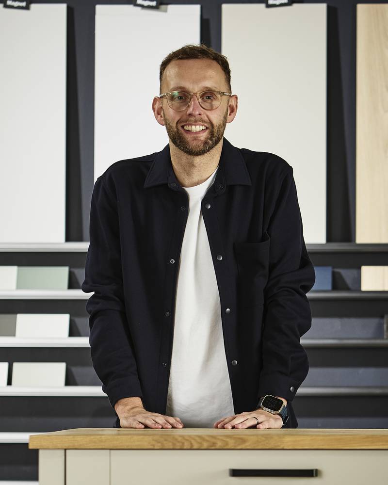 Magnet's product expert Matty Jones, pictured in our kitchen cabinet testing facility, with a range of kitchen cabinet colours and textures in the background.
