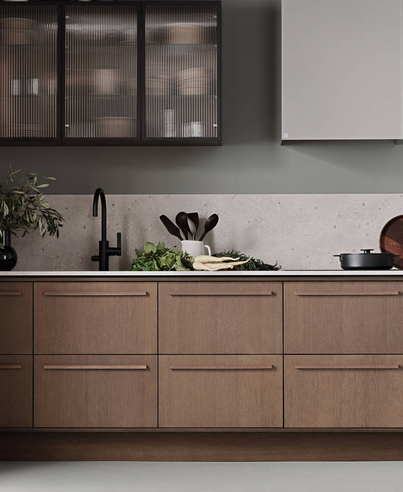 Køkken Forever Oak fra INVITA, mørk eg køkkenskabe med massiv tre mørk eg håndtag, komposit bordplade, sort armatur og vitrineskab med riflede glas i tynd, sort aluminiumsramme