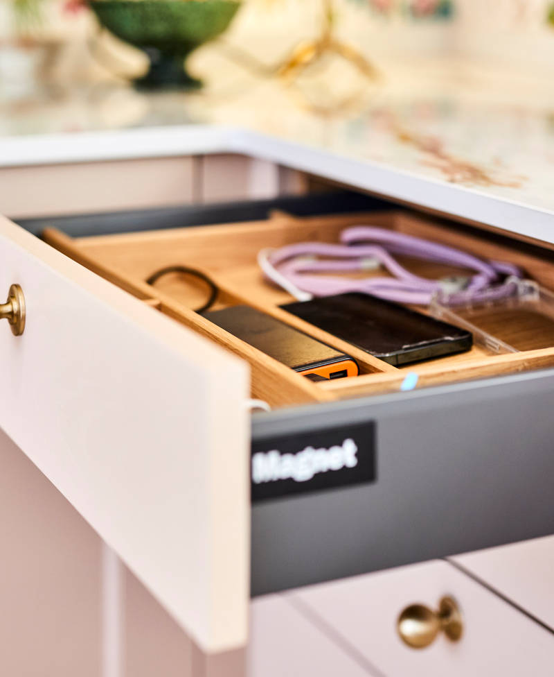 Close-up view of opened Ludlow Chalk blush front drawer from Magnet with wooden insert and electronic devices charging.