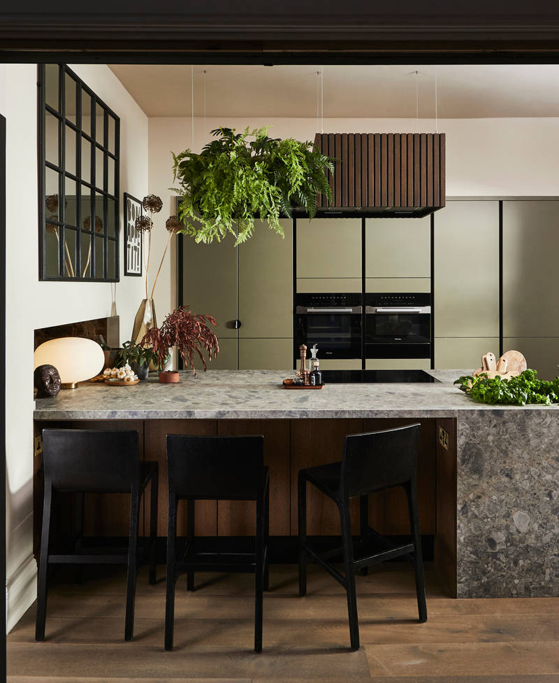 View through opened dark wood doors of the biophilic Dramatic neutral Balmoral Soho and Nordic Nature kitchen from Magnet, matching dark wood chairs by kitchen island bar seating area.