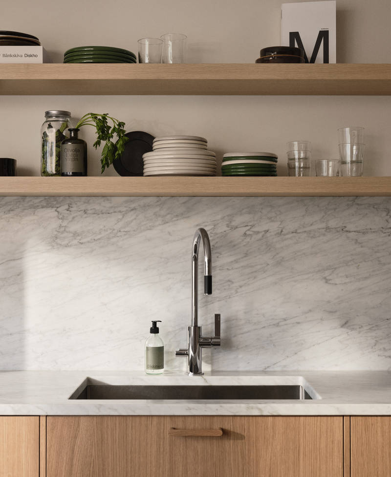 Öppna trähyllor ovanför köksbänk i Siri Barjes ek-kök från Marbodal, med bänkskiva och stänkskydd i marmor, svart diskho och blandare från Tapwell.