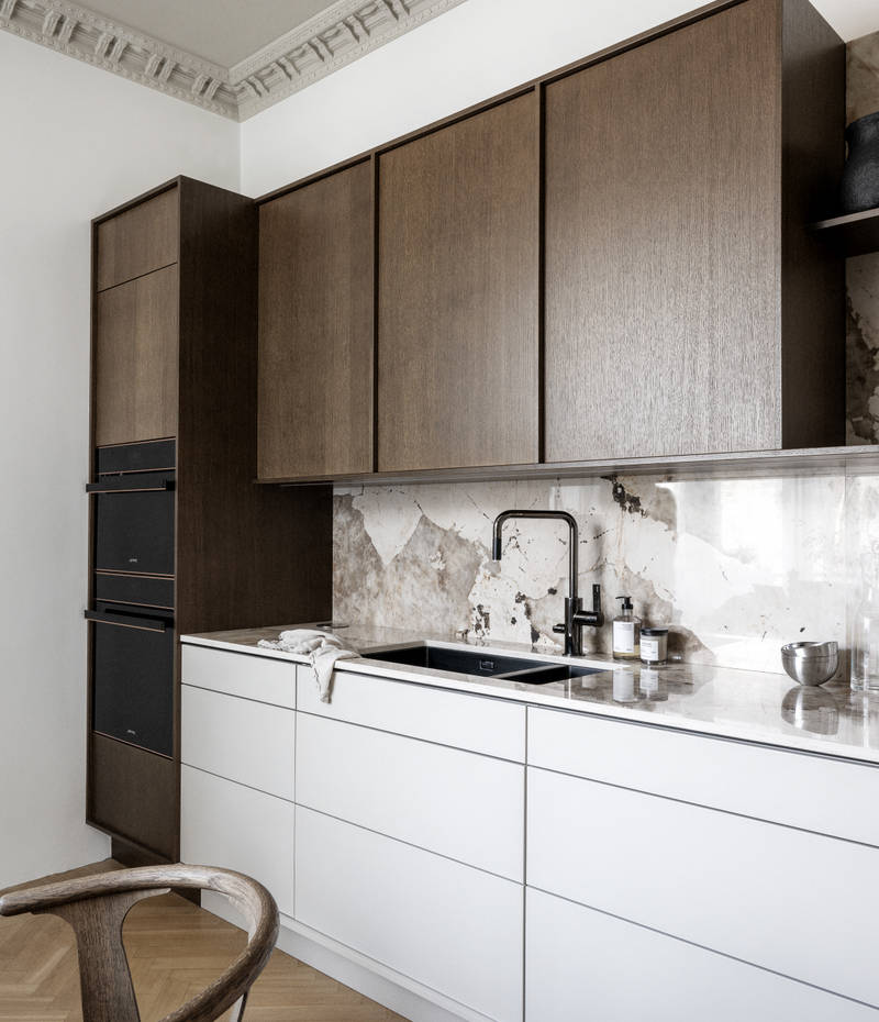 Køkken med en kombination af køkkenbænk i beige Arkitekt Plus Sand med overskabe og højskabe i Signatur Ekbacken fineret egetræslåge i brunbejdset fra Marbodal, bordplade og stænkplade der matcher og åbne væghylder i brunbejdset eg finer.